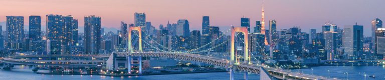 View of Tokyo’s Rainbow Bridge illuminated at dusk with the city skyline and Tokyo Tower in the background.