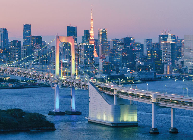 View of Tokyo’s Rainbow Bridge illuminated at dusk with the city skyline and Tokyo Tower in the background.