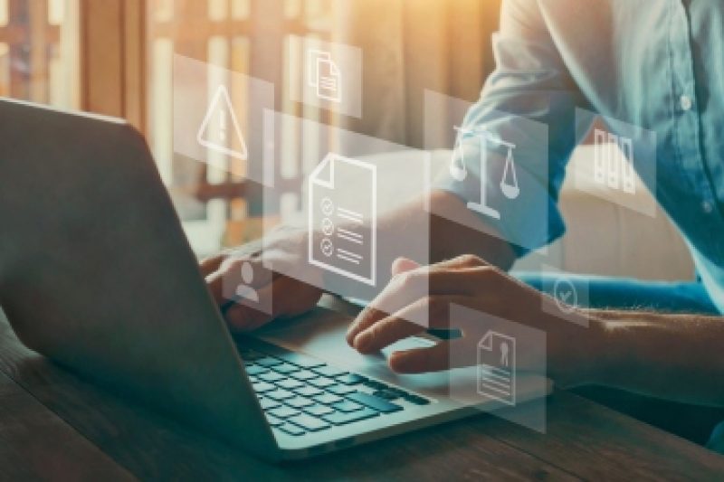 Person working on a laptop with digital icons of documents, compliance, and legal symbols overlaid to represent data management and regulatory processes.